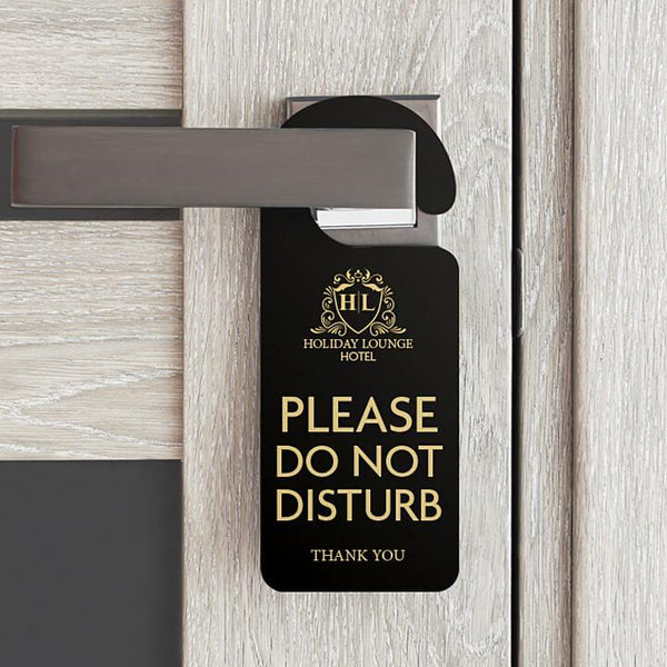 Black 'Please Do Not Disturb' door hanger on modern silver door handle with wooden door background