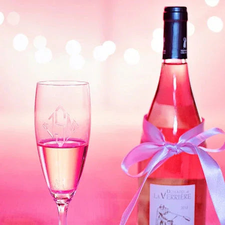 Bottle of pink rosé wine with a white ribbon and a partially filled wine glass against pink bokeh background