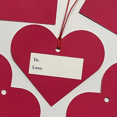 Red heart-shaped Valentine’s gift tag with white label reading To: Love: on white background