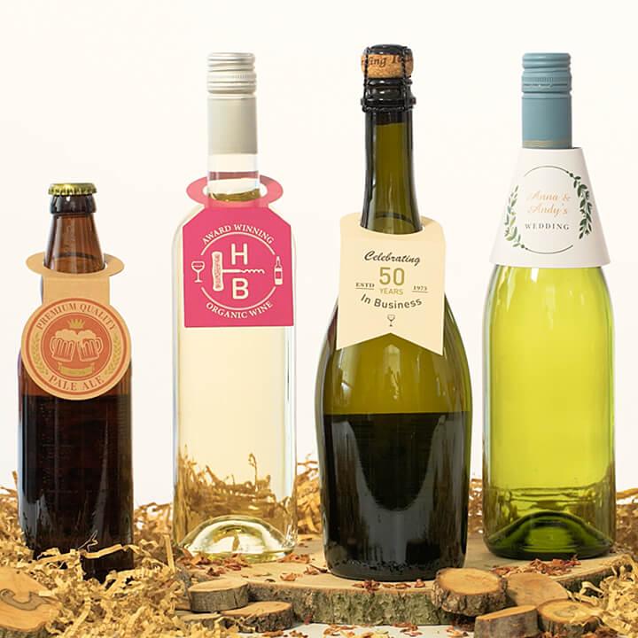 Four bottles with personalised bottleneck tags on wood slice and straw, including pale ale, white wine, sparkling wine, and wedding bottle