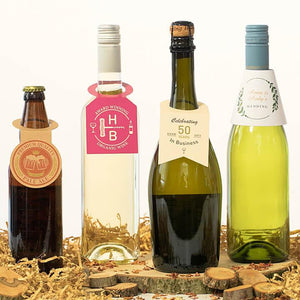 Four bottles with personalised bottleneck tags on wood slice and straw, including pale ale, white wine, sparkling wine, and wedding bottle