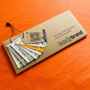 Sample pack of eco-friendly hang tags on a brown envelope with black string, on orange background